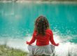 back view of woman sitting on a rock by a body of water and meditating