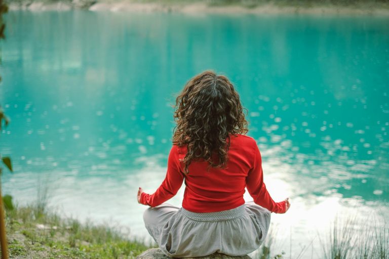 pexels-photo-20367722 back view of woman sitting on a rock by a body of water and meditating