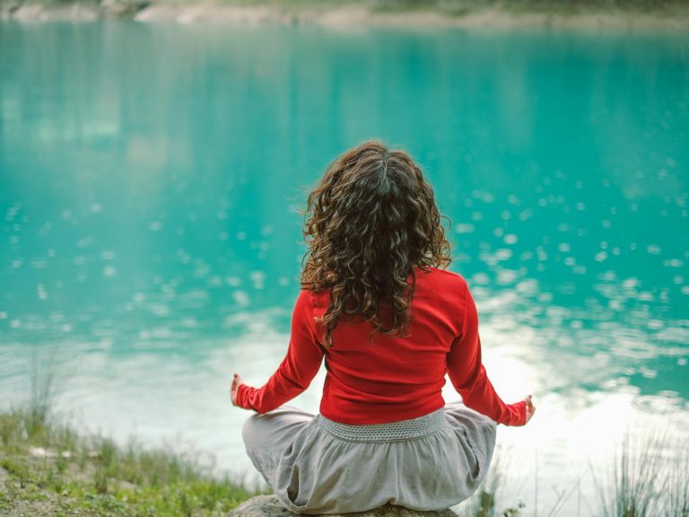 pexels-photo-20367722 back view of woman sitting on a rock by a body of water and meditating