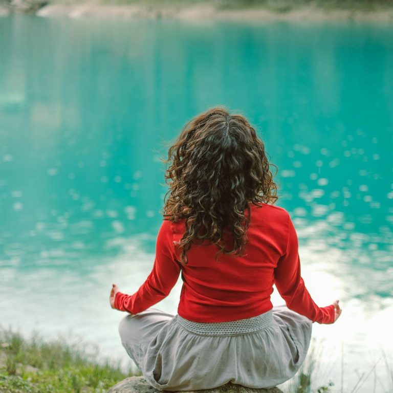 pexels-photo-20367722 back view of woman sitting on a rock by a body of water and meditating